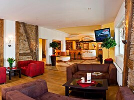 A hotel lobby with red sofas, a reception desk, a bar area, and a television screen.