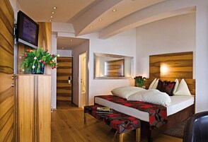 A modern hotel room with a bed, a television, a wooden cabinet, and a hallway leading to another room.