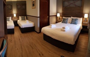 A hotel room with a large bed, two smaller beds, wooden flooring, and bedside lamps. - Clachaig Inn (Ballachulish)