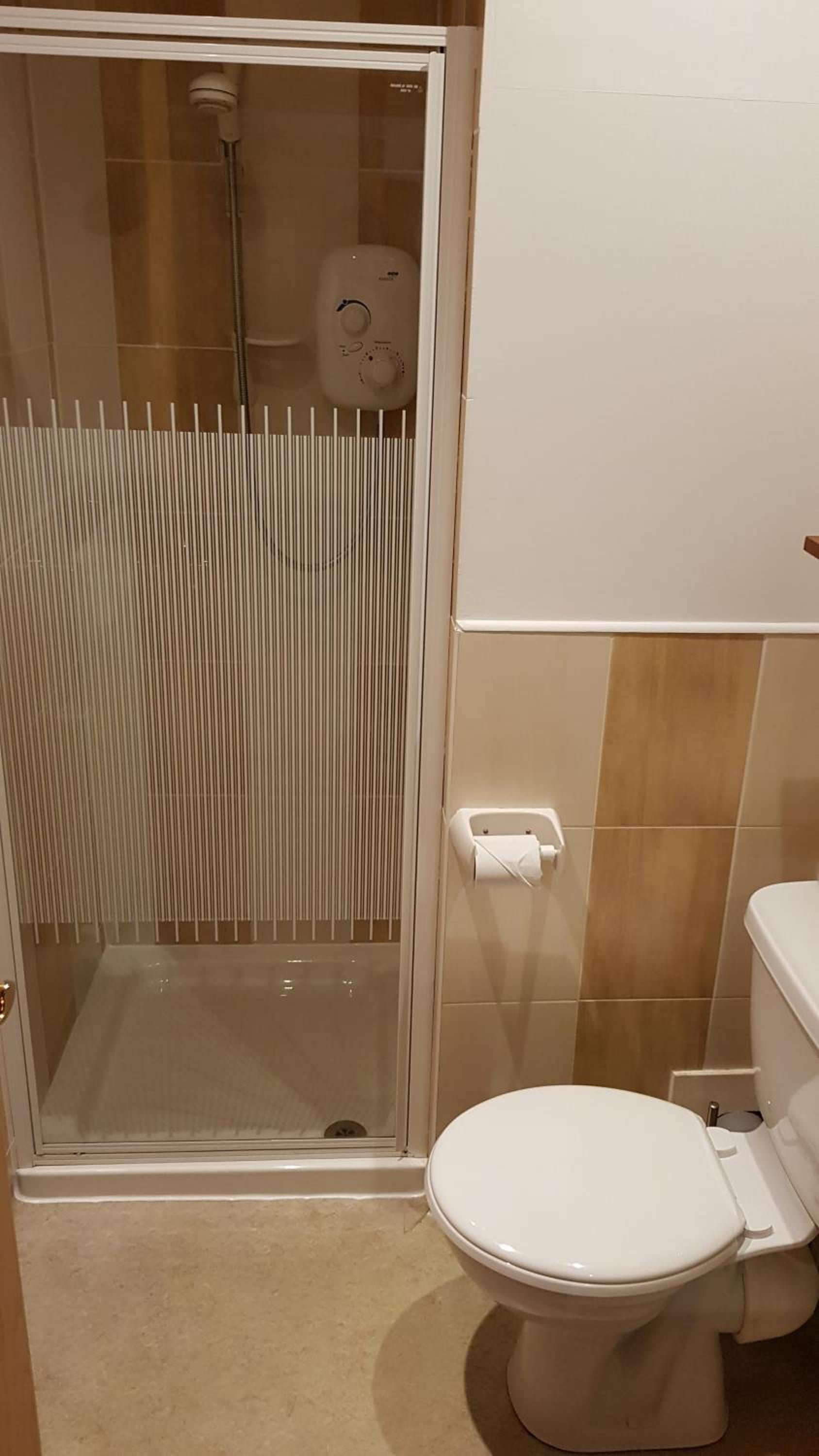 Un baño con inodoro, cabina de ducha y soporte para papel higiénico.