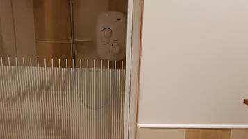 Un baño con inodoro, cabina de ducha y soporte para papel higiénico.