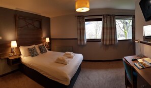 A hotel room with a large bed, bedside lamps, a desk with a chair, a television, and a window with curtains. - Clachaig Inn (Ballachulish)