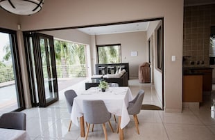 Comedor con mesa lista para cuatro personas, zona de cocina y vista a un balcón con vegetación.