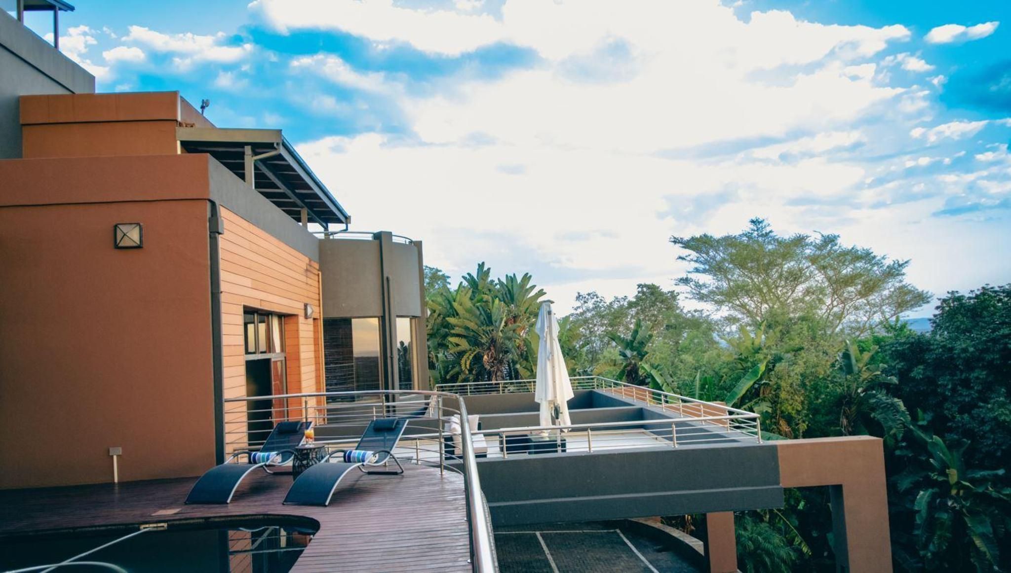 A rooftop terrace with lounge chairs, a pool, and a view of the surrounding greenery.