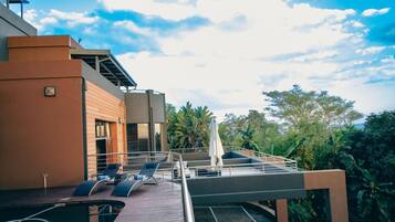 A rooftop terrace with lounge chairs, a pool, and a view of the surrounding greenery.