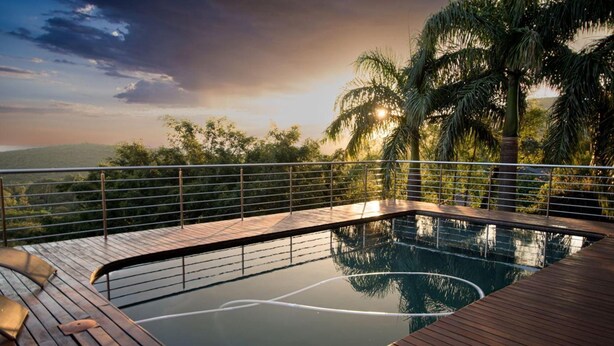 A pool with a wooden deck and metal railing, surrounded by palm trees and a view of the landscape. - Schimper View Boutique Guest House (Louis Trichardt)