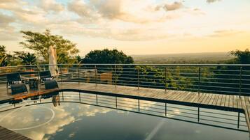 A pool area with a wooden deck, lounge chairs, and a view of the landscape.