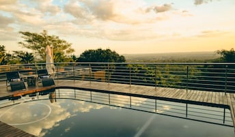 Zona de piscina con terraza de madera, sillones de descanso y vistas al paisaje.