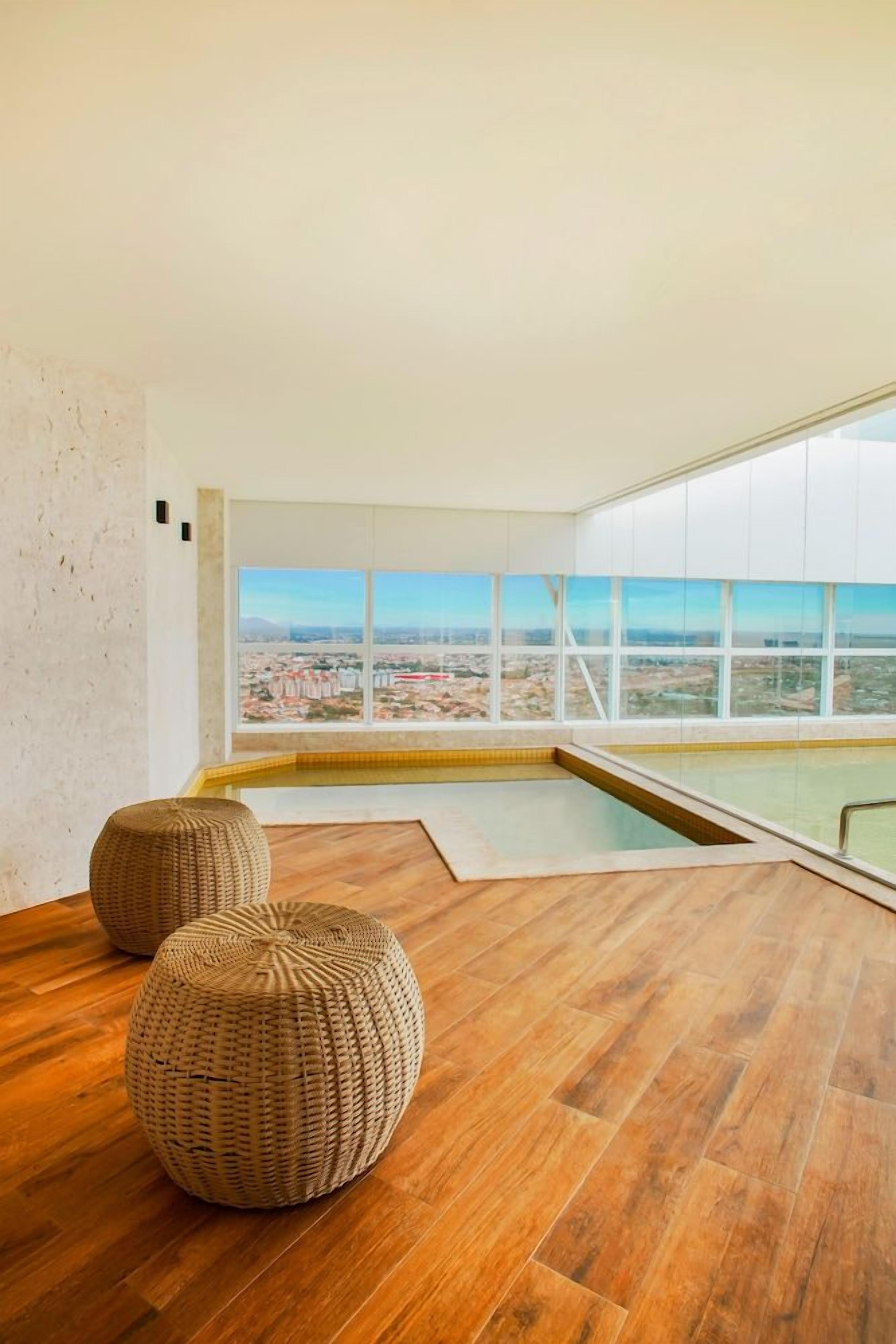 Un interior moderno con un amplio ventanal, una piscina y dos otomanas tejidas.