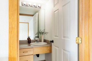 Un bagno con un mobile bagno in legno, uno specchio illuminato, un lavandino e una porta con maniglia in ottone.