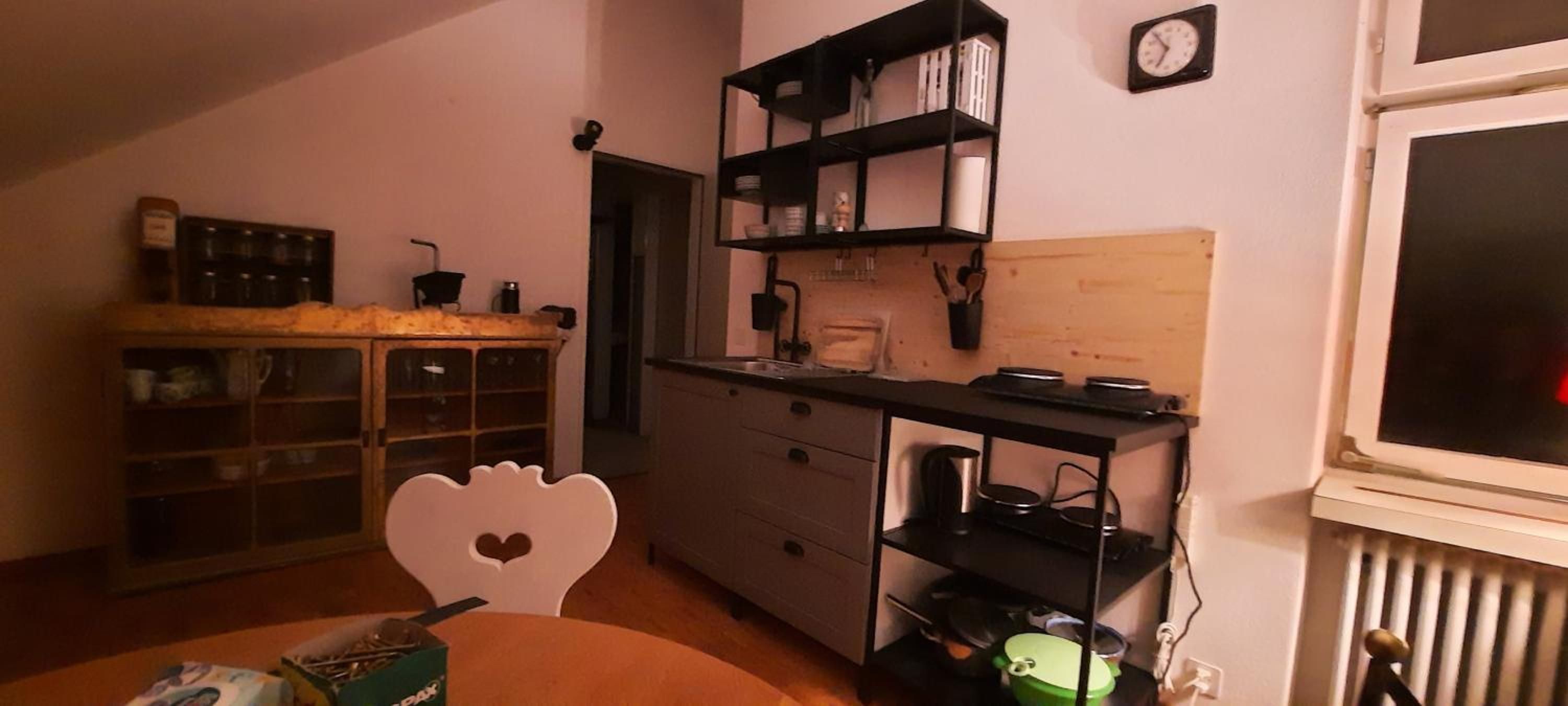 A compact kitchen with a dining area, featuring a heart-shaped chair, a small table, and a radiator.