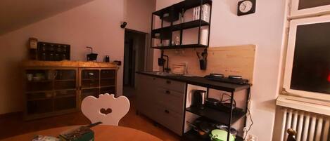 A compact kitchen with a dining area, featuring a heart-shaped chair, a small table, and a radiator.
