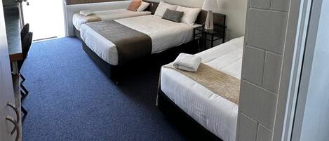 A hotel room with three beds, a desk, and a chair.