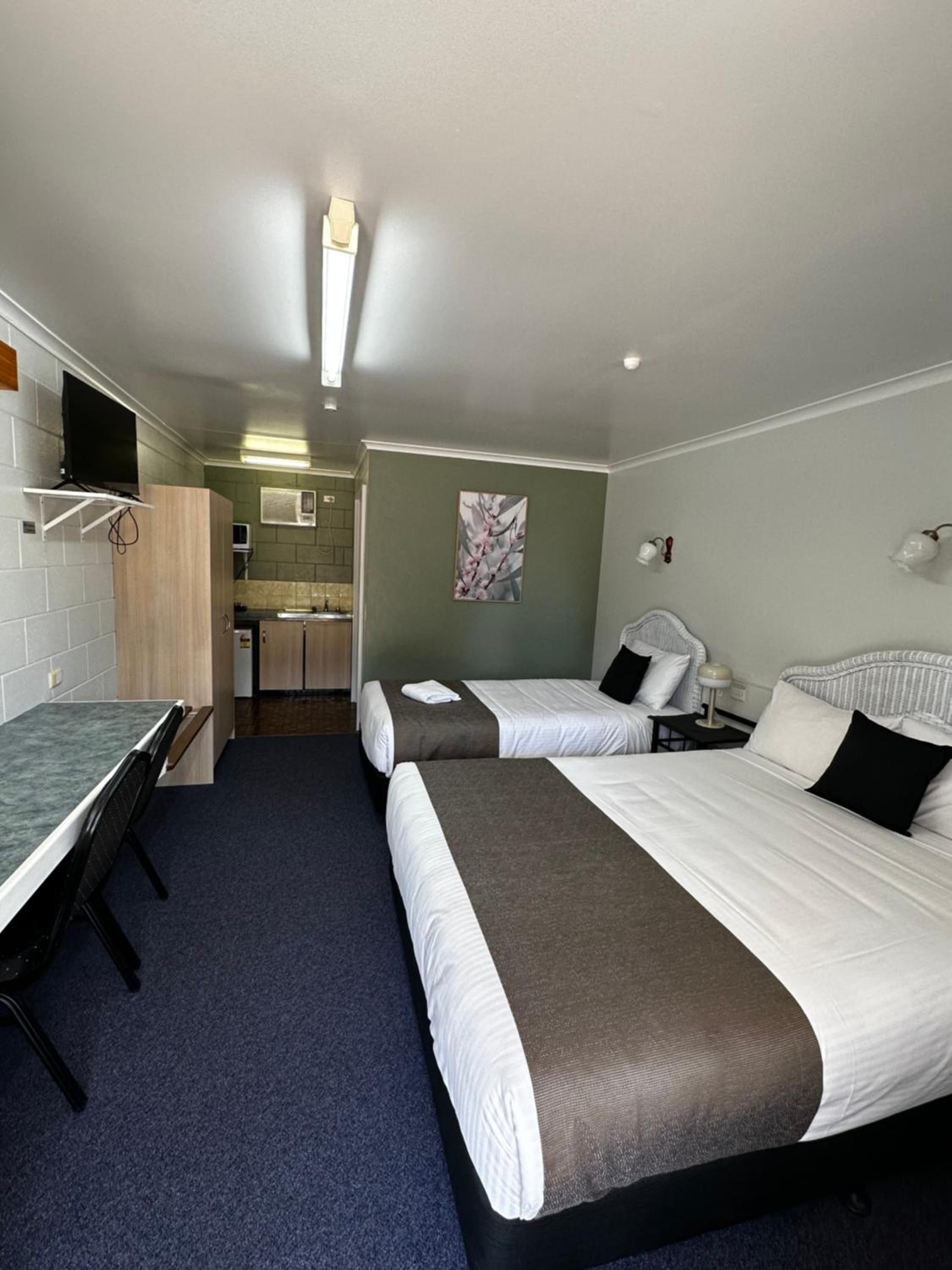 A hotel room with two beds, a desk, a chair, a TV, and a kitchenette.