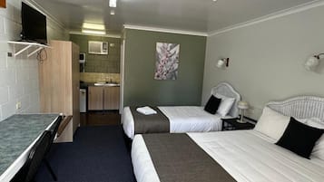 A hotel room with two beds, a desk, a chair, a TV, and a kitchenette.
