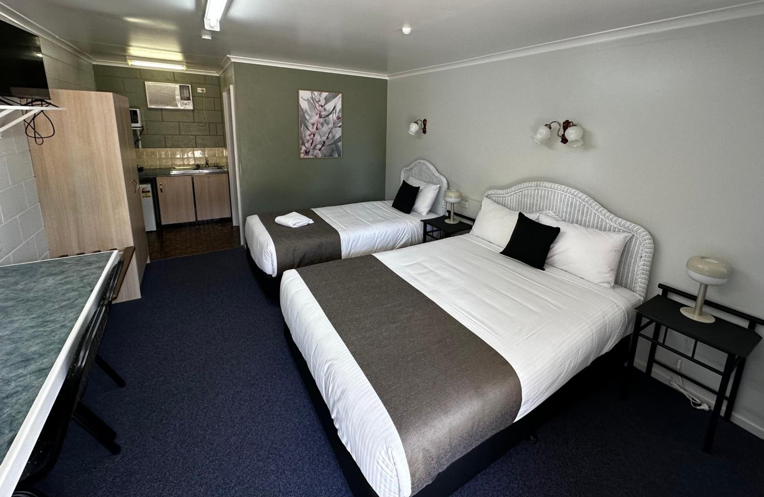 A hotel room with two beds, a small kitchenette, and a bathroom.