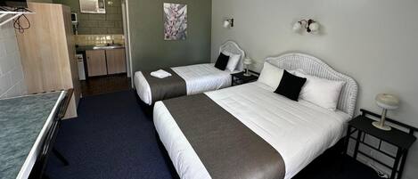 A hotel room with two beds, a small kitchenette, and a bathroom.