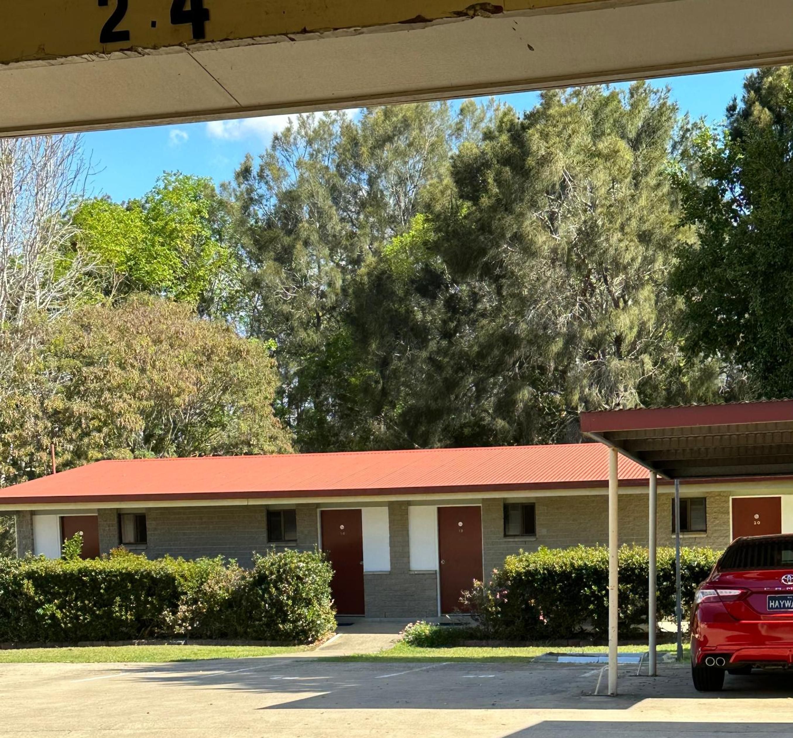 A motel with a red roof, a covered parking area, and a red car parked in front.