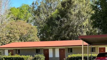 A motel with a red roof, a covered parking area, and a red car parked in front.