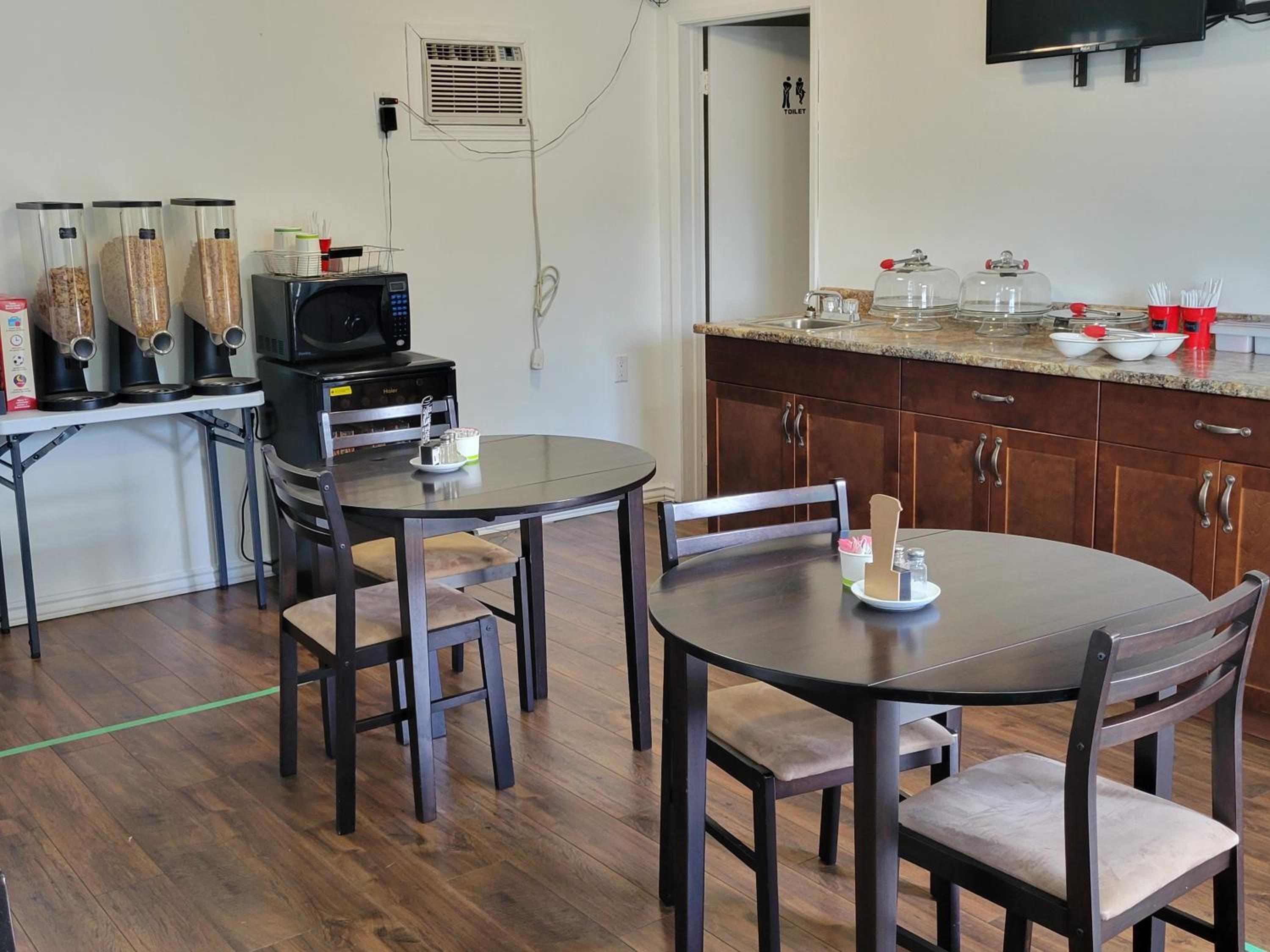 A compact kitchen with a microwave, a coffee maker, and a toaster. There are two dining tables with chairs, and a sink with a countertop.