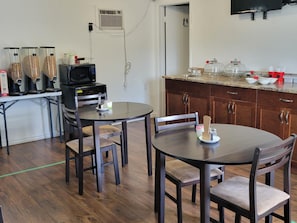 Une cuisine compacte équipée d’un four à micro-ondes, d’une machine à café et d’un grille-pain. On y trouve deux tables à manger avec des chaises, ainsi qu’un évier avec un plan de travail.