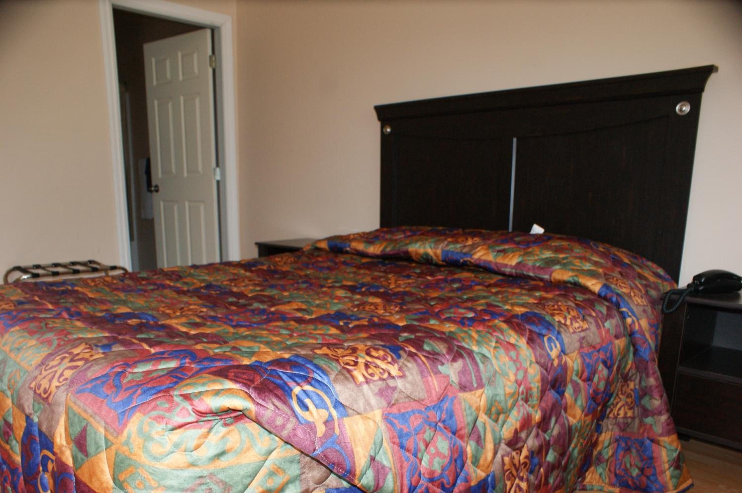 A bedroom with a bed, a door, and a nightstand with a phone.