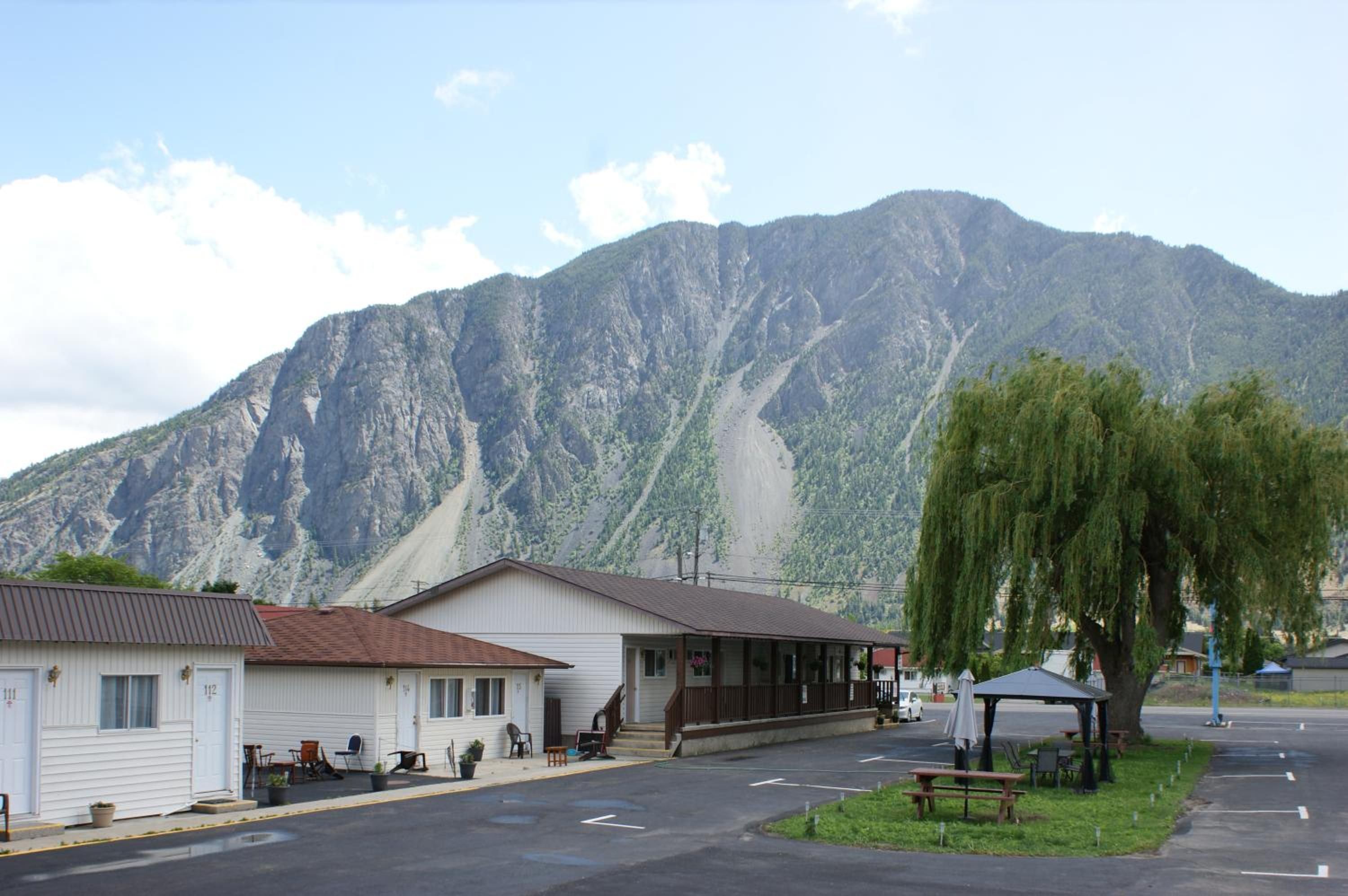 A motel with a mountain backdrop, outdoor seating, and a covered picnic area.