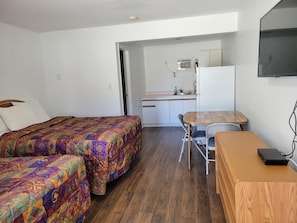 Une chambre avec deux lits, une petite kitchenette, une table à manger et un téléviseur.