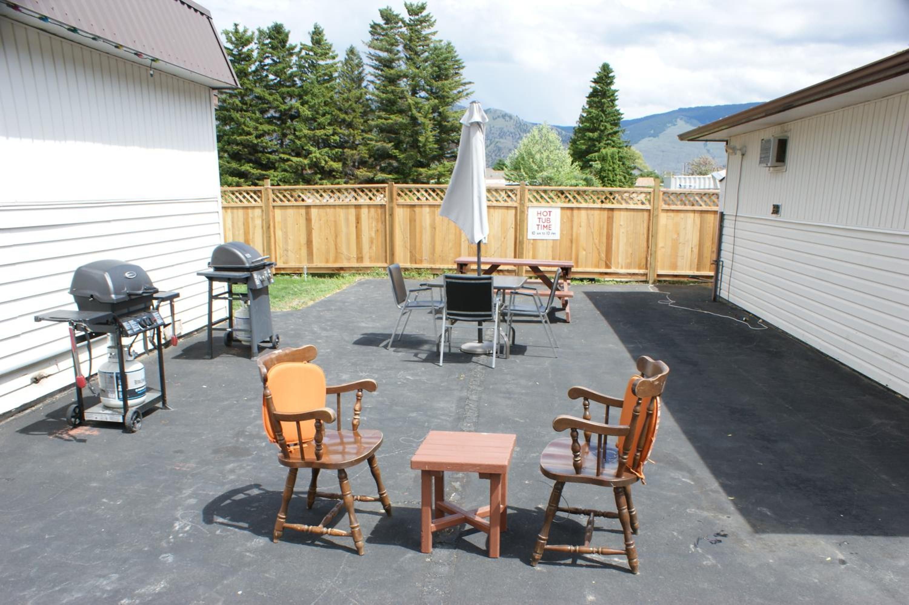 An outdoor patio area with a barbecue grill, two wooden chairs, a small table, and a covered umbrella.
