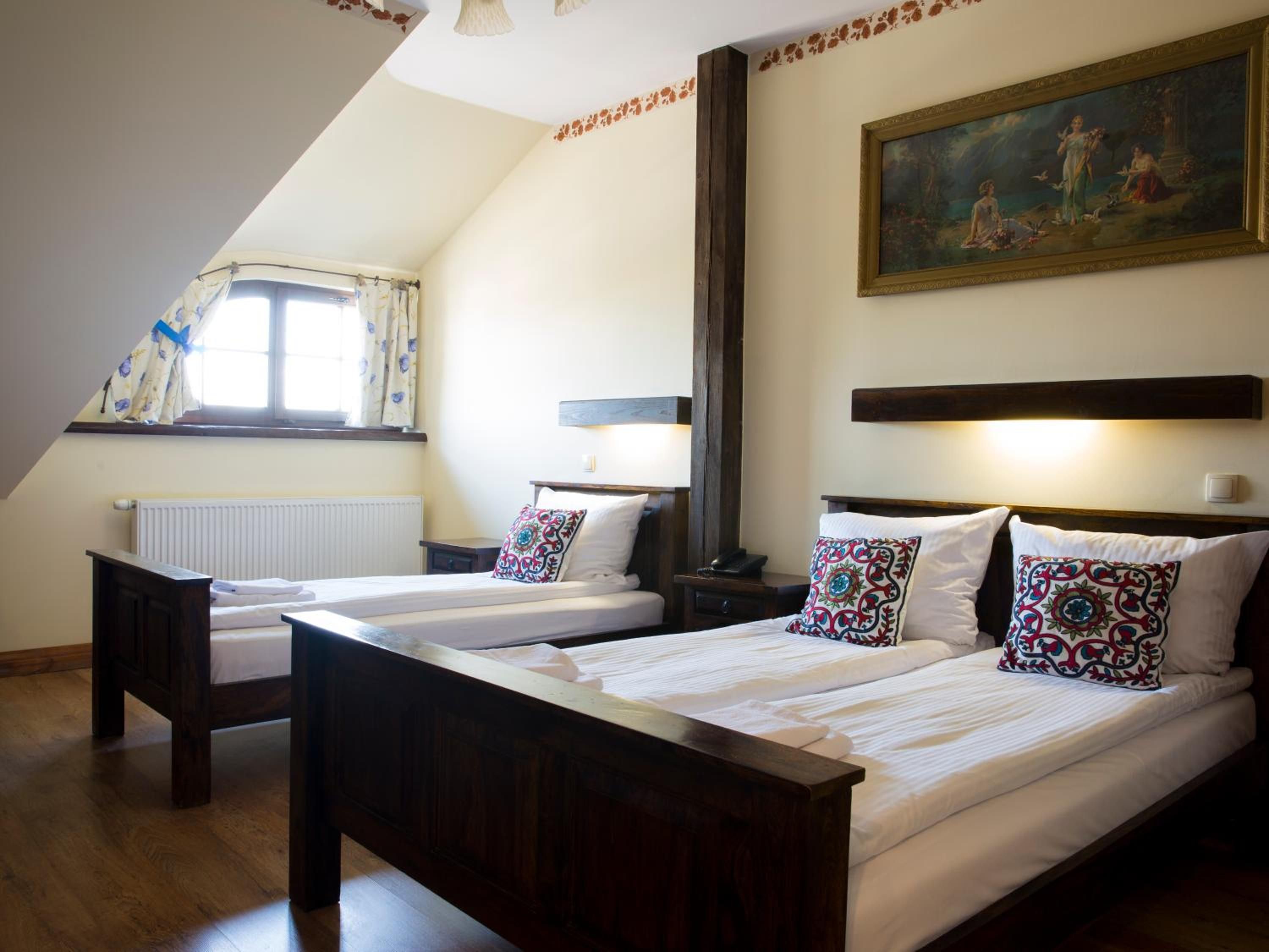 Una habitación con dos camas individuales, una ventana con cortinas, un radiador y un cuadro en la pared.