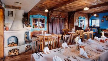 Un comedor rústico con mesas y sillas de madera, una chimenea y una pared azul con detalles decorativos.
