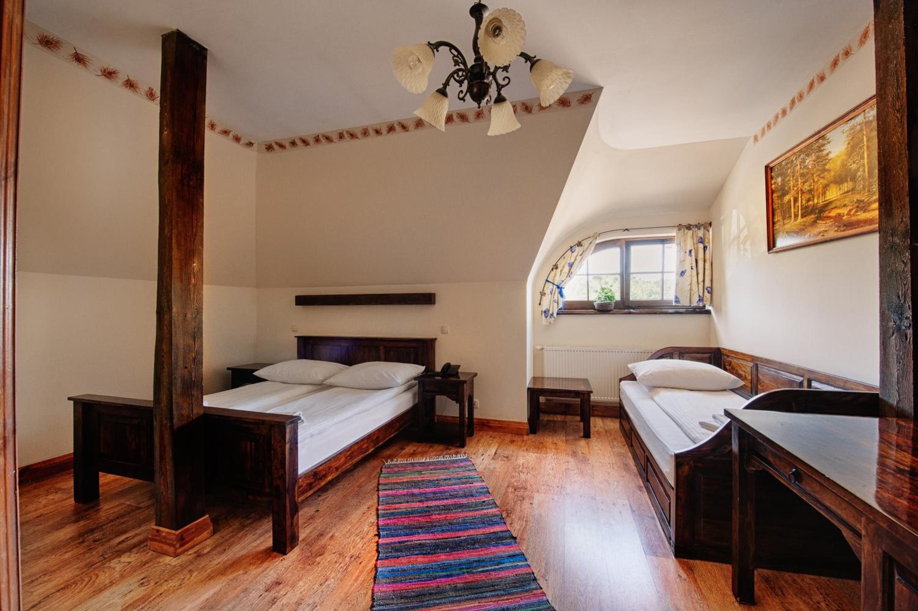 A bedroom with two single beds, a wooden floor, a striped rug, a ceiling fan, and a window with curtains.