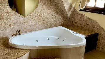 Un baño moderno con una bañera independiente, paredes de mosaico de piedra y un ventanal con cortinas.