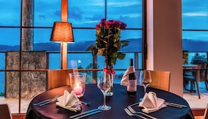 A dining table set for two with a candle, wine glasses, and a vase of flowers.