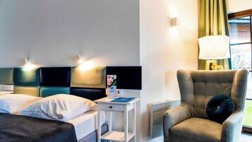 A hotel room with a bed, a bedside table, a chair, a lamp, and a window with curtains.