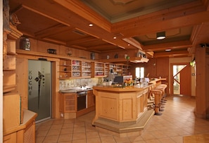 A spacious kitchen with wooden cabinets, a large island, and a bar area with stools. - Alpengasthof Grimmingblick (Irdning-Donnersbachtal)