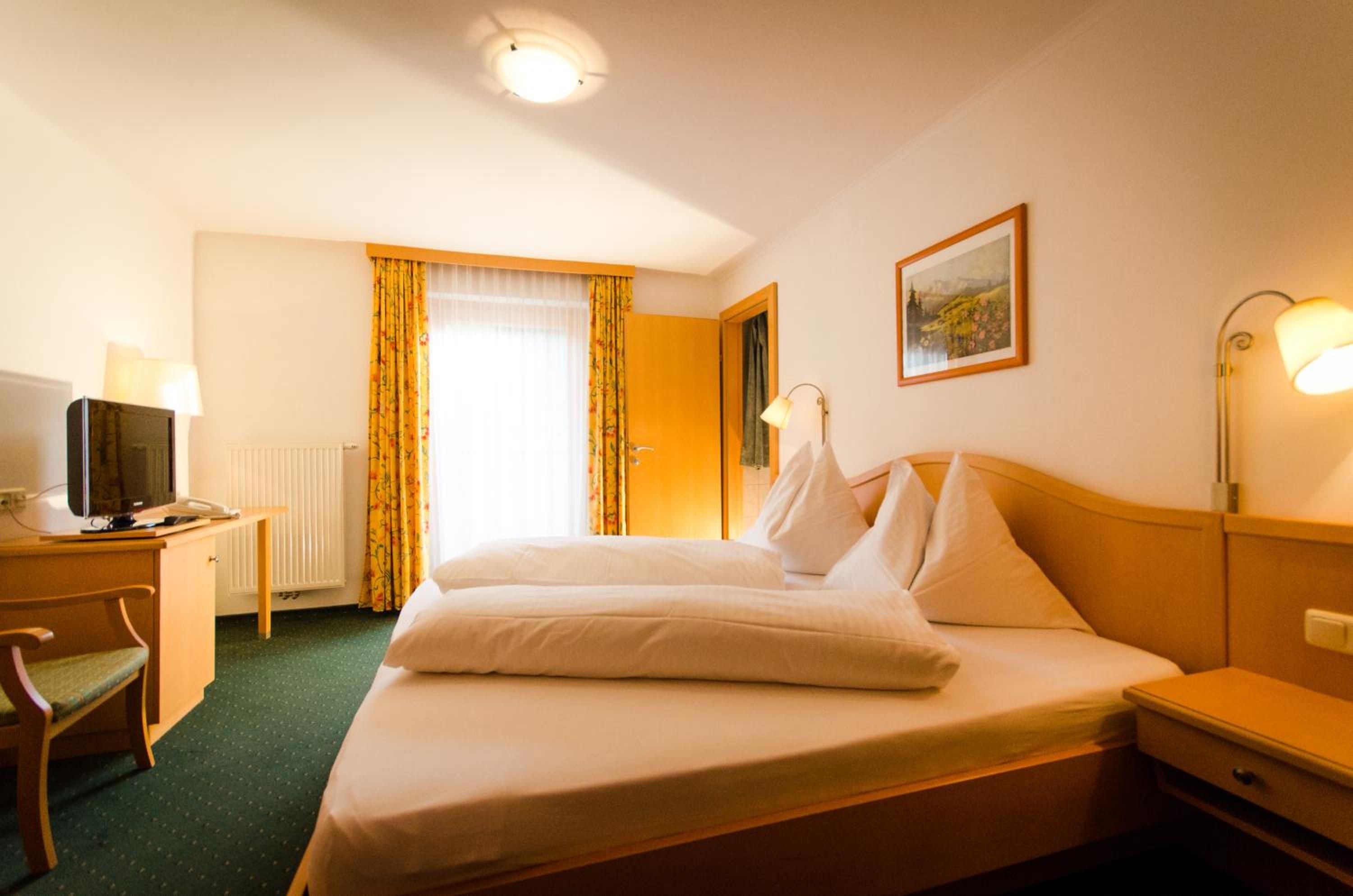 A hotel room with a bed, a desk with a computer, a chair, a lamp, and a painting on the wall.