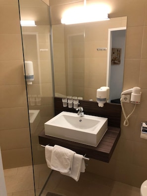 Un baño moderno con cabina de ducha de vidrio, un lavabo blanco, un espejo y un perchero para toallas.