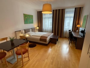 Habitación de hotel con cama, escritorio, silla y una pequeña mesa con una planta.