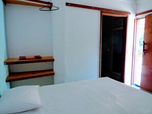 A bedroom with a bed, wooden shelves, a hanging light, and a door leading to a balcony.