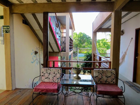 An outdoor seating area with two chairs and a table, a staircase leading to a balcony, and a sign indicating an exit. - Tribo De Gaia (Conceicao da Barra)