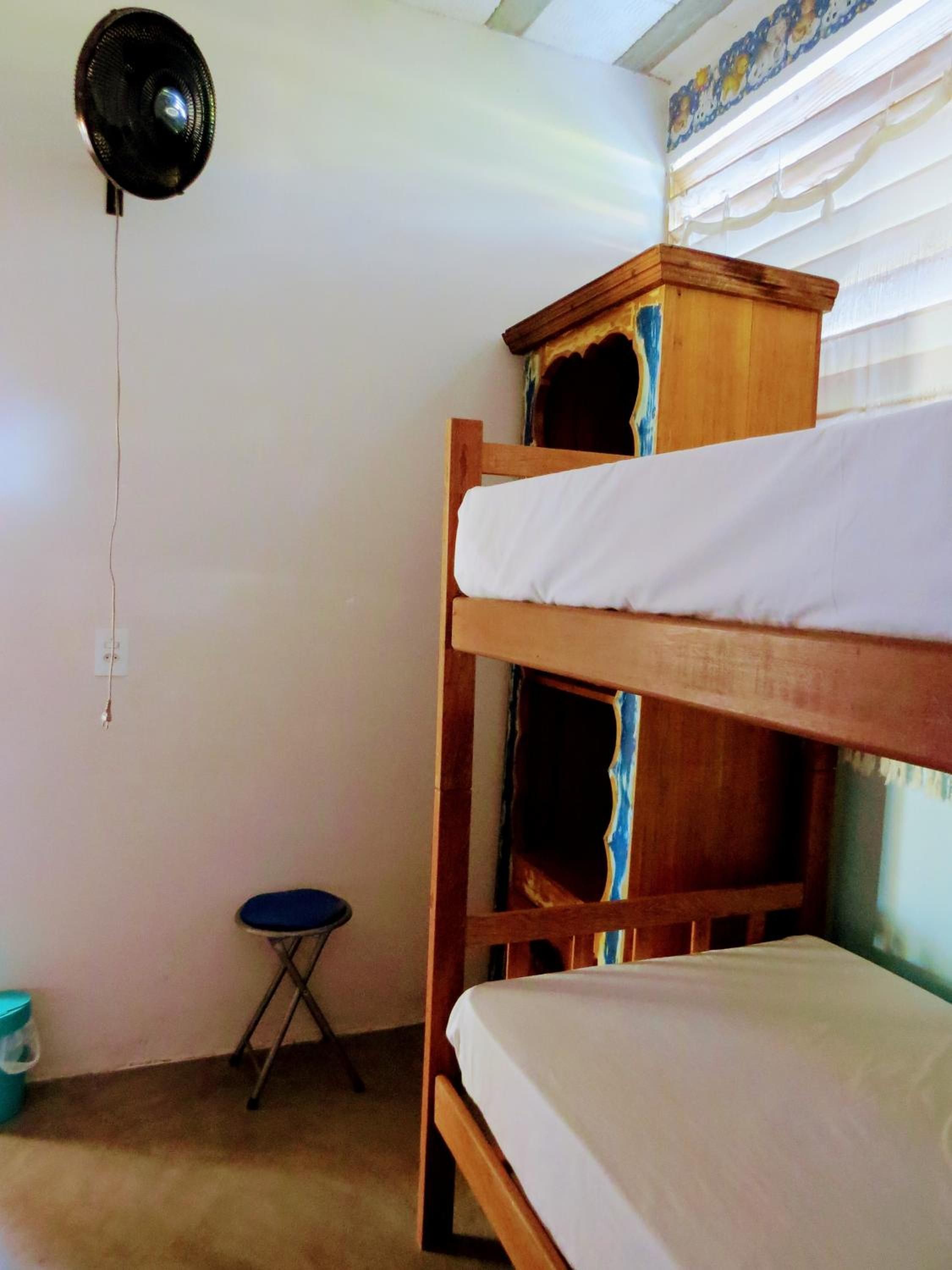 A bunk bed with a wooden headboard, a small stool, and a wall-mounted fan.
