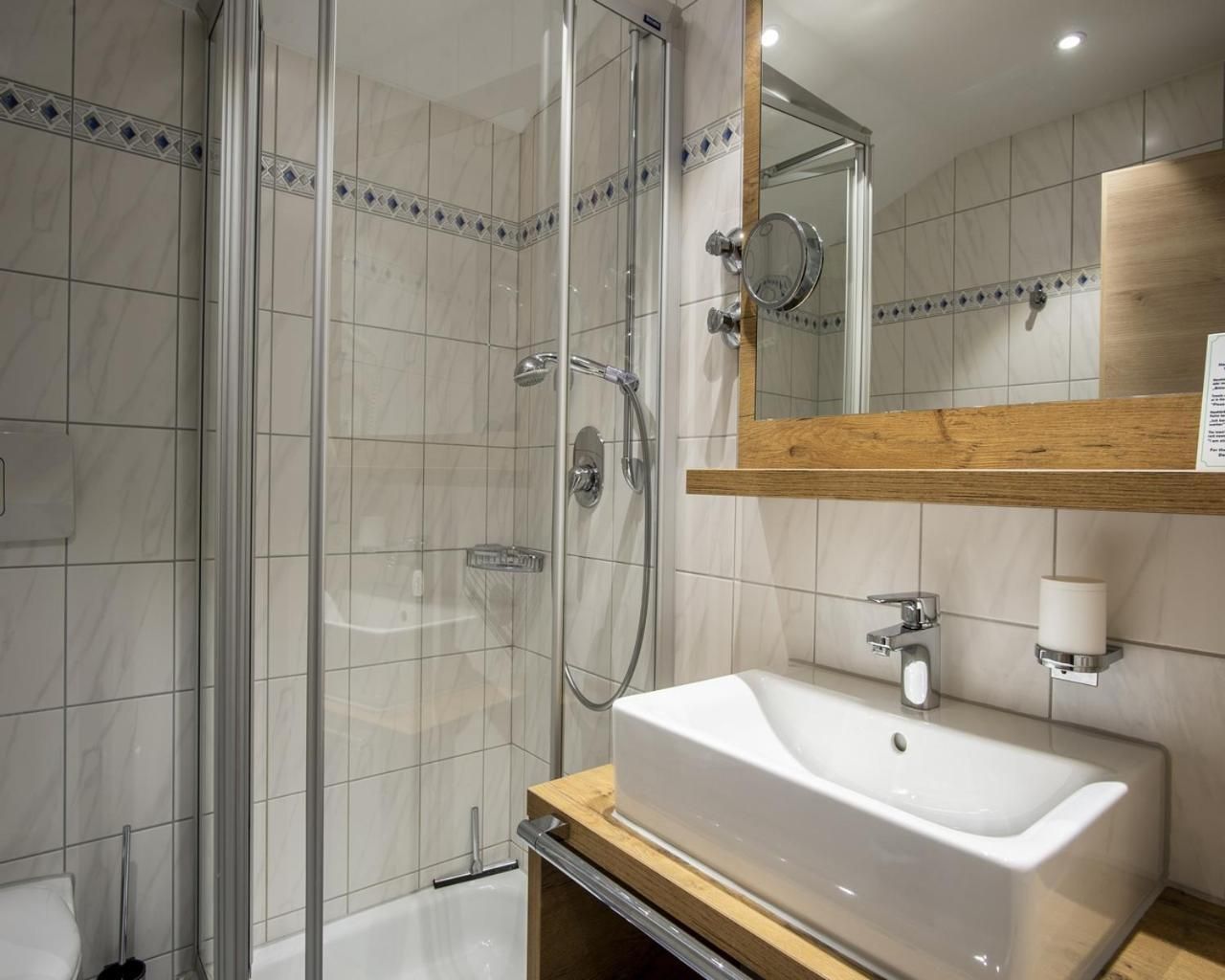 Ein modernes Badezimmer mit einer gläsernen Duschkabine, einem weißen Waschbecken und einem Holzwaschtisch.