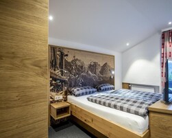Quarto com cama de madeira, mesa de cabeceira, TV na parede e um grande mural.
