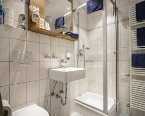 Un baño moderno con un lavamanos blanco, una ducha con cerramiento de vidrio y una bañera blanca.