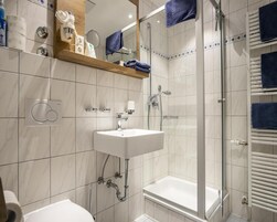 Un baño moderno con un lavamanos blanco, una ducha con cerramiento de vidrio y una bañera blanca.