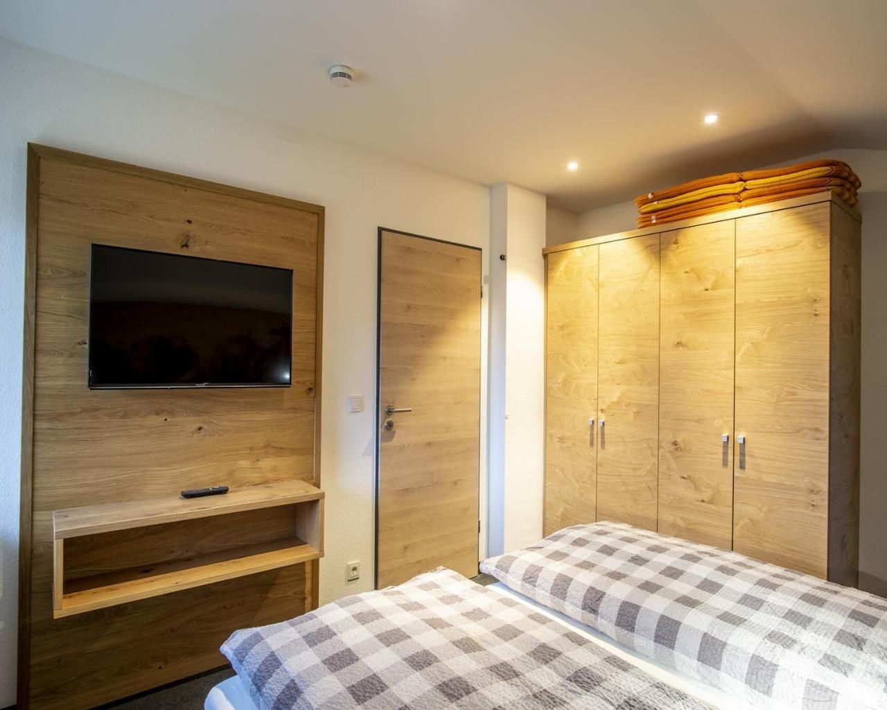 A bedroom with a TV mounted on the wall, a wardrobe, and a bed with a checkered bedspread.