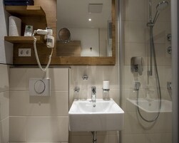 Casa de banho moderna com lavatório branco, secador de mãos, cabine de duche em vidro e espelho.
