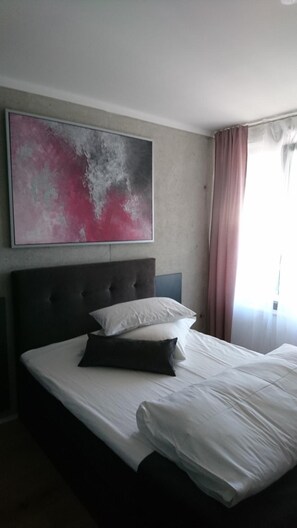 A hotel room with a large bed, a headboard, a wall-mounted abstract painting, and a window with curtains. - Haus 7 - Boardinghouse (Kornwestheim)