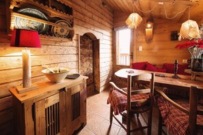 Un interior rústico de madera con una zona de comedor, un sofá rojo y un ventanal que proporciona luz natural.